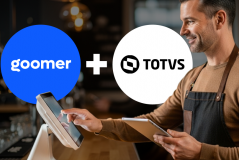 Imagem de um barista sorridente atendendo clientes, com os logotipos do Goomer e TOTVS ao fundo, destacando a parceria entre as marcas