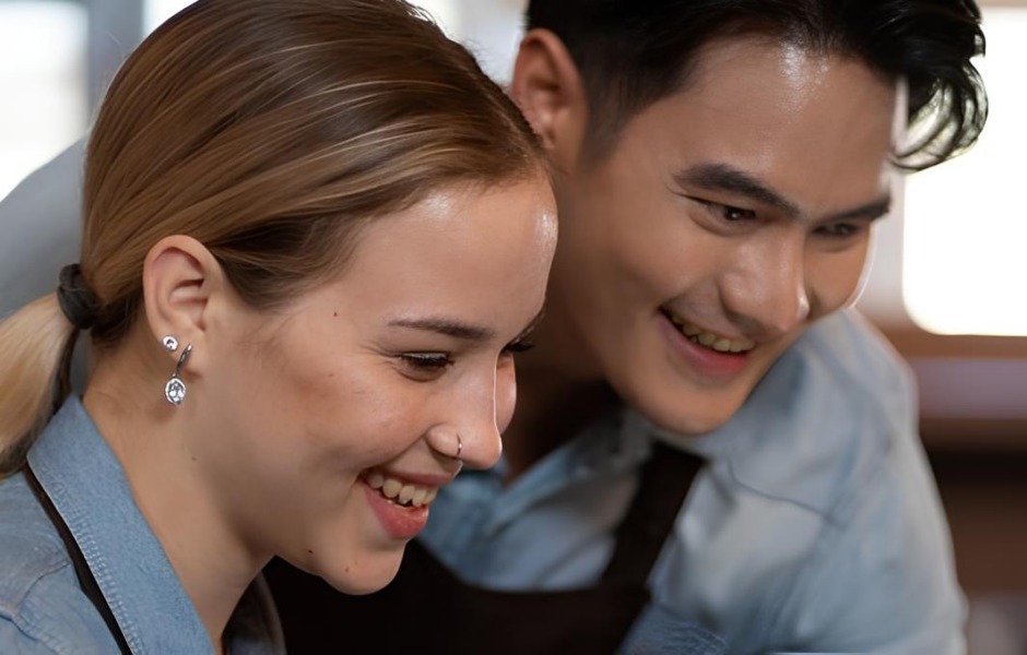 Close de um homem e uma mulher sorridentes, usando aventais, olhando para algo à frente.