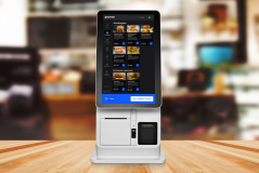 Menino usando uma máquina de pedidos de comida digital em um restaurante, com a tela exibindo várias opções de hambúrgueres e refeições para fazer pedidos online.