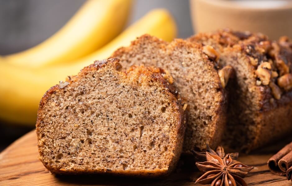 Delicioso bolo de banana fatiado, com nozes e canela, perfeito para o café da manhã ou lanche da tarde, em fundo com bananas.