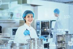 Imagem de uma cozinheira em uma cozinha industrial moderna, com utensílios de cozinha e tecnologia visível.
