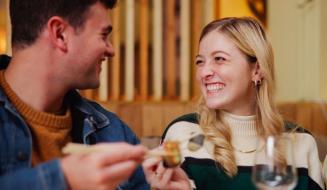 Casal sorridente desfrutando de um momento romântico em restaurante, com destaque para a mulher com cabelo loiro e o homem com cabelo castanho, em um ambiente acolhedor.