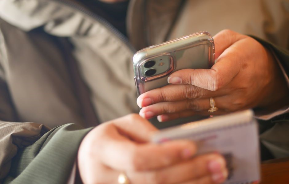 Pessoa usando um smartphone para tirar uma foto ou enviar uma mensagem, com foco na mão e o aparelho, fundo suave e desfocado.