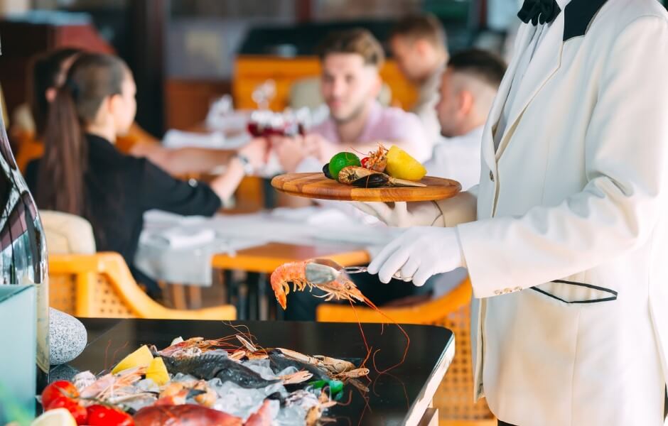 Um garçom em um restaurante elegante serve um prato com frutos do mar, limões e vegetais para os clientes.